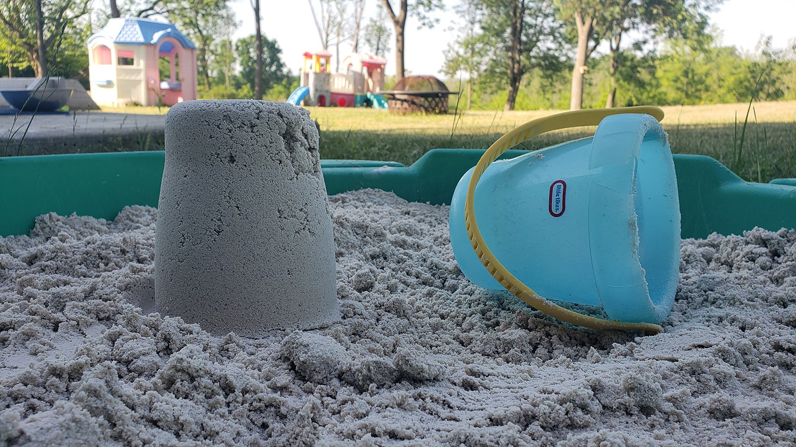 A small sandcastle stands next to the bucket used to make it.