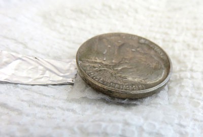 A nickel is placed on top of a penny that is covered with a wet paper towel square