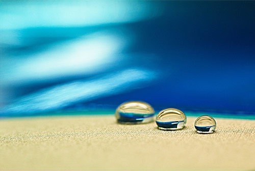 Three different sized water droplets rest side-by-side on a flat surface