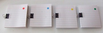 Four stacks of paper each held with a binder clip are marked with different colored dots