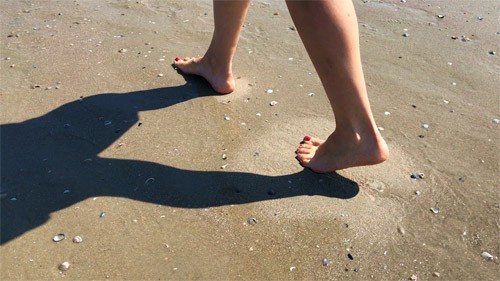 Close up photo of two feet walking across wet sand
