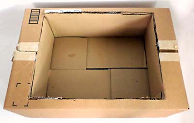 A smaller cardboard box is inserted into an opening in the lid of a larger cardboard box