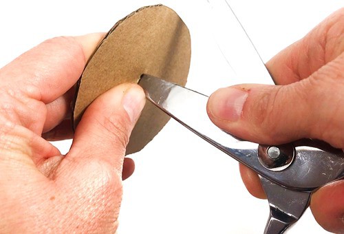 Person punching a hole into the center of a cardboard circle with scissors.