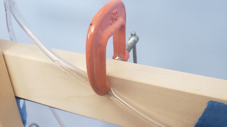 A c-clamp squeezes the tubing against the wooden frame in order to reduce water flow. 