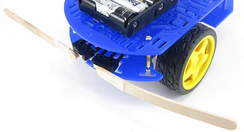 Two popsicle sticks are attached to individual lever switches at the front of an object avoiding robot