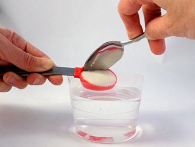 Two spoons are used to drop yogurt into a water and sodium alginate solution in a single mass