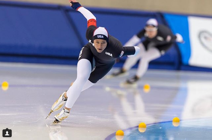 A woman in a USA speedskating suit skating in an ice rink