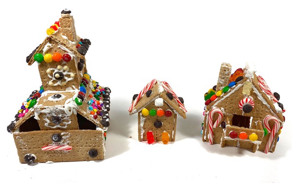 Three houses made from Graham crackers are standing next to each other. Each house is decorated with candy. 