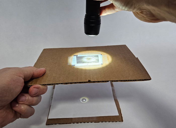 A pinhole projector being used indoors with a flashlight.