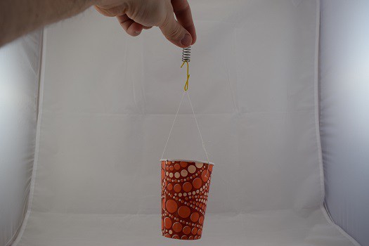 A paper cup hanging from a string, paper clip, and spring.