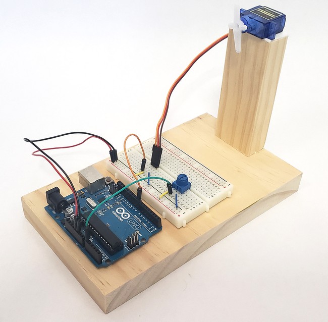 Arduino and breabdoard sitting on a piece of wood, with an additional taller piece of wood supporting the motor 