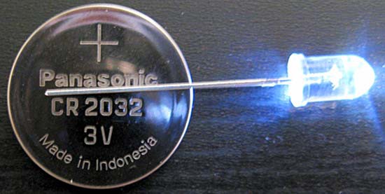 Coin battery inserted between the prongs on a white LED light bulb so that it remains lit