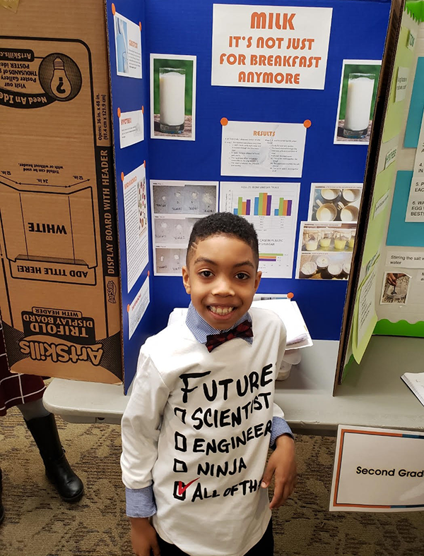 A student standing in front of a science fair display board