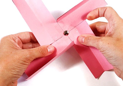 Paper pinwheel made from four paper strips with a thumbtack through its center. 