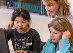 A teacher helping two students in front of a computer