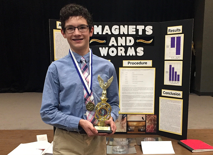 A student holding a trophy in front of a science fair display board
