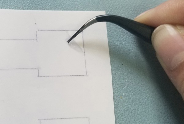 A close-up picture of using tweezers to peel vinyl off of the glossy temporary tattoo backing paper. 