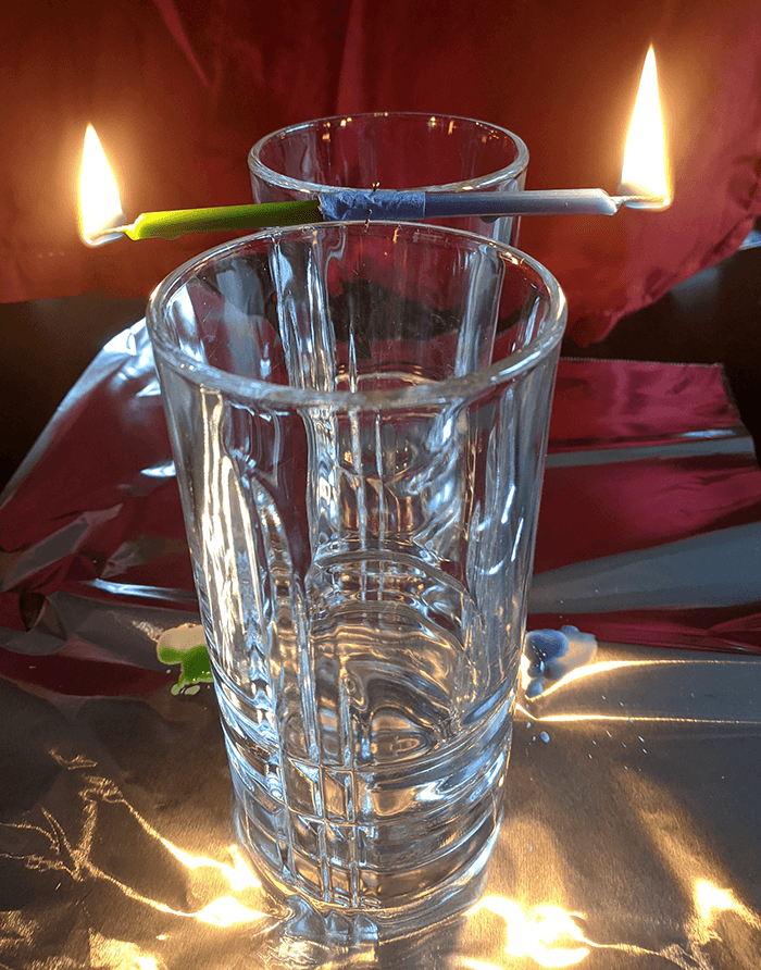 Lit candles taped end to end balanced between two drinking glasses
