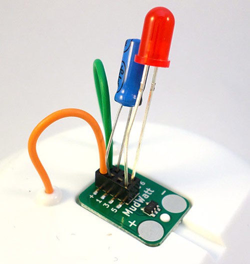 An orange and green wire stick through a lid and connect to a circuit board with a blue and red LED