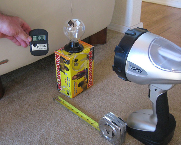 Person using a tachometer to measure the rotation rate of vanes of a radiometer exposed to a spot light