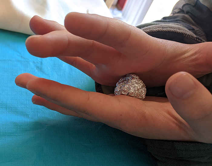 Student hands holding small aluminum foil ball that has been rolled to be used as the core of a model virus