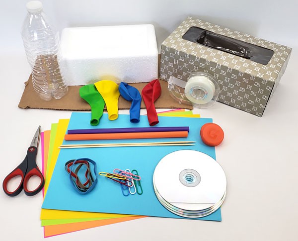 A tissue box, foam block, plastic bottle, cardboard, paper, CDs, rubber bands, paperclips, plastic straws, balloons and tape
