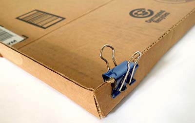 Binder clips are used to hold the corners of a cardboard lid together