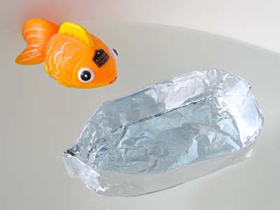 A toy goldfish and an aluminum foil boat float side by side in water