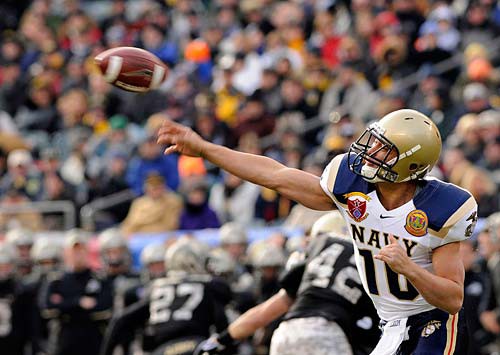 A quarterback for the U.S Navy football team throws a football in a crowded stadium