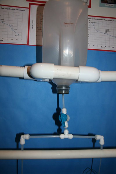 An upside plastic bottle drains into a T-shaped valve that splits the water into two separate streams