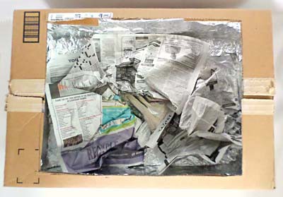 The inside of a cardboard box is lined with aluminum foil and filled with crumpled balls of newspaper