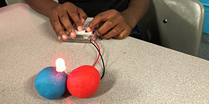 A child assembles a circuit made from an LED, battery pack and two balls of conductive play dough
