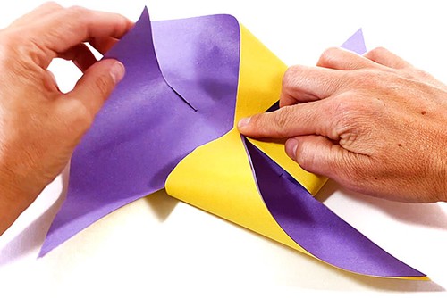  Hands folding  cut paper square into a pinwheel.