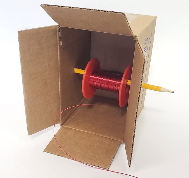 A small cardboard box with a pencil poked through two of its sides and a wire spool on the pencil 