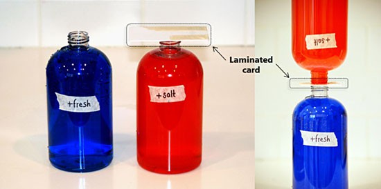 A thin laminated card is used to stack a glass bottle of red liquid mouth-to-mouth with a glass bottle of blue liquid