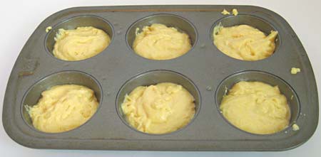Yellow batter is evenly distributed into the six cups of a muffin pan