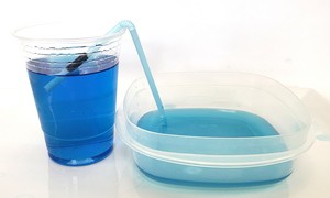 A straw siphoning water from a plastic cup into a shorter plastic container. 
