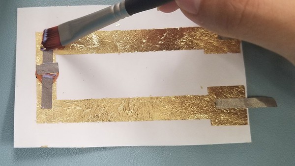 Applying a thin layer of sealer on the metal leaf circuit with a paint brush. 