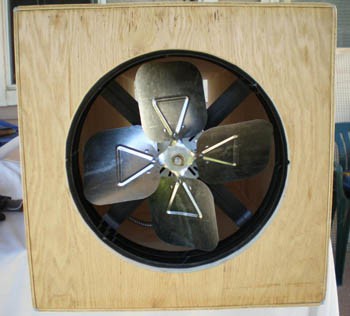 A fan rests in a circular hole cut from the center of a square wooden panel