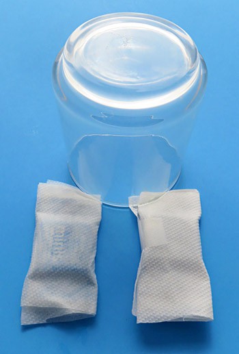 A wet and dry paper towel are wrapped around two identical chocolate candies and are held in place by an upside-down glass