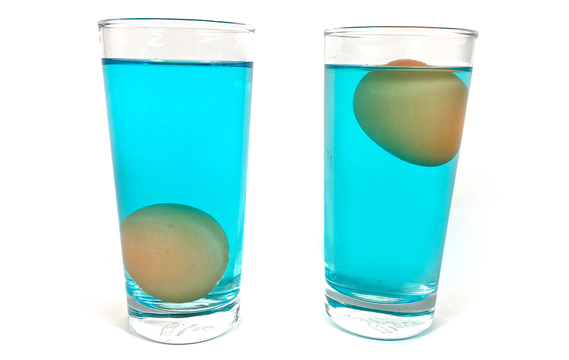 Two cups, each with an egg floating in salt water