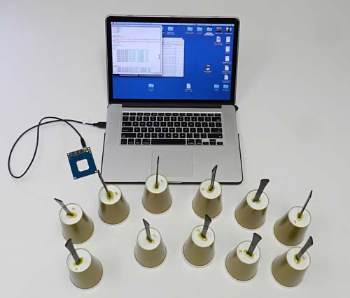 Eleven handbells made of paper cups sit in front of a RFID reader that is connected to a laptop