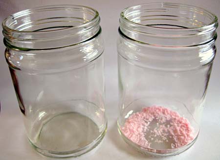 An empty glass jar next to a glass jar that contains a small amount of pink powder