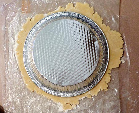 An aluminum pie pan is placed upside down on a circle of rolled out dough