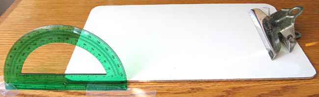 A protractor is taped perpendicular to a tables surface and aligned with a clipboards edge at the focal point