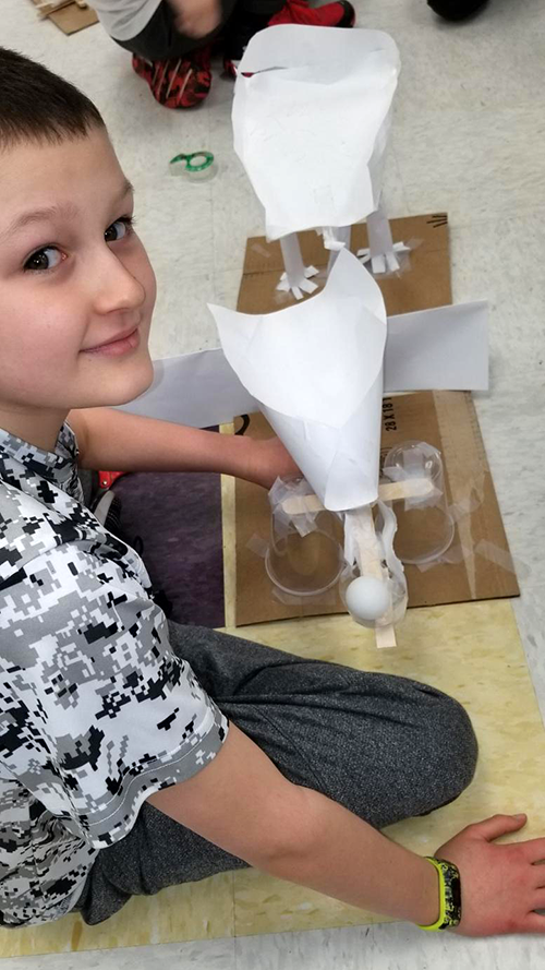 A student sitting next to a paper ball launcher and catcher