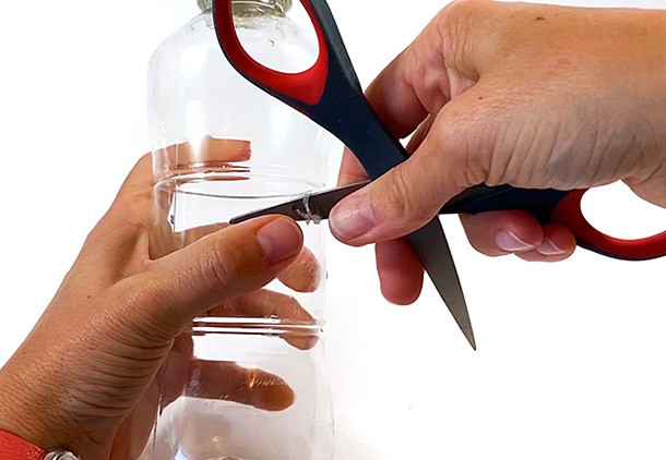 Hands holding scissors that pierce a hole through the side of a plastic bottle.