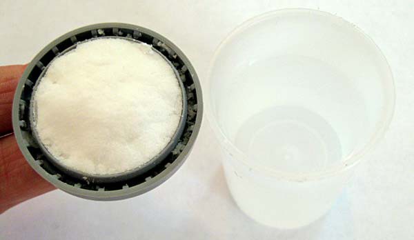 Baking soda packed into the inside of a film canister lid next to a film canister filled with vinegar