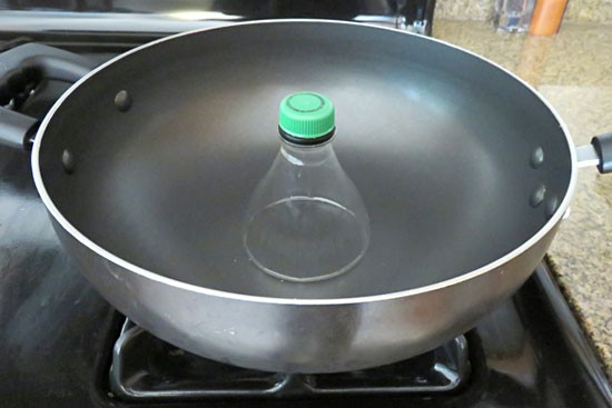 The cut neck of a plastic bottle rests in a frying pan to melt the cut plastic edge