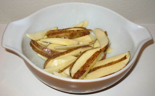 A bowl of raw potato wedges that have been dried and seasoned with oil and salt